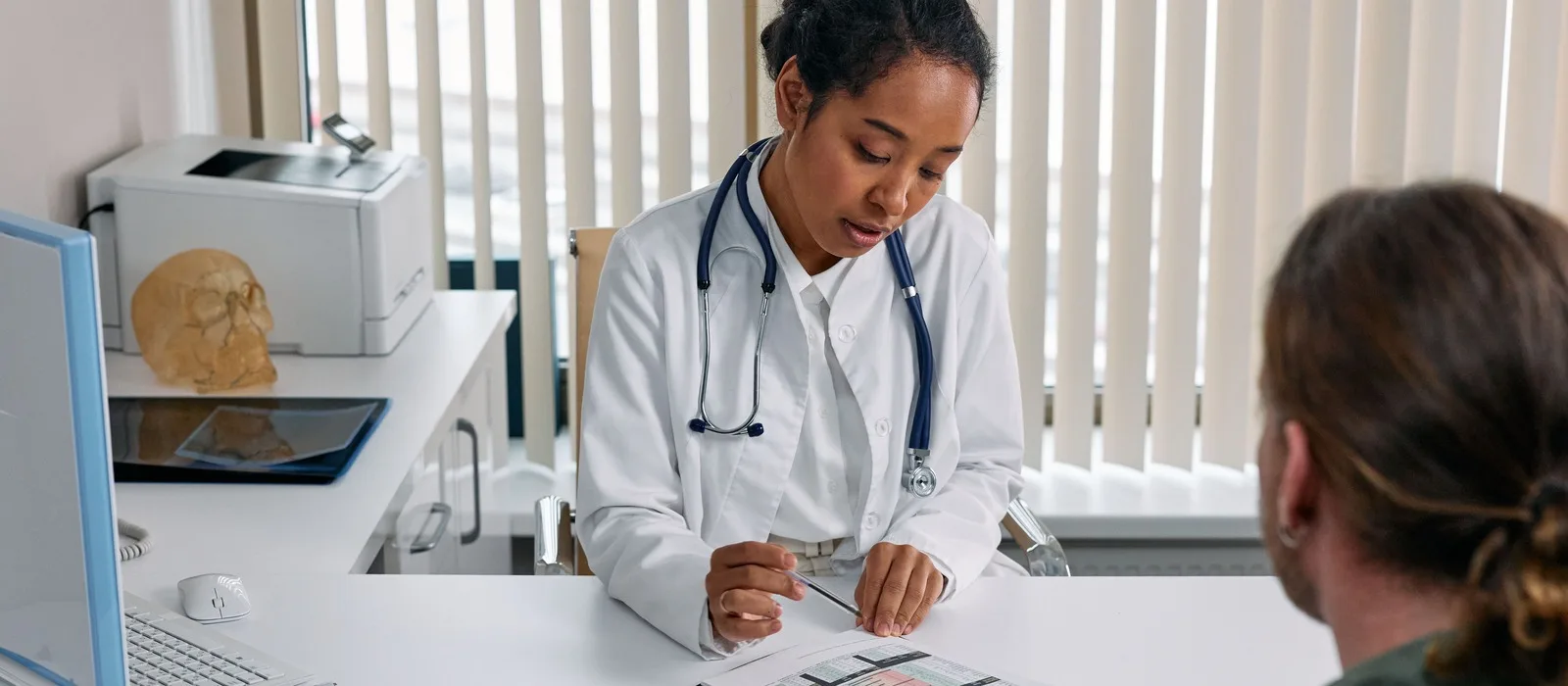 Doctor reviewing medical notes with a patient at a clinic desk.