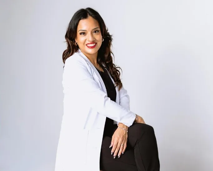 Portrait of Mical Pacheco, MSN, APRN, PMHNP-BC, wearing a white lab coat and seated in a clinical studio setting.