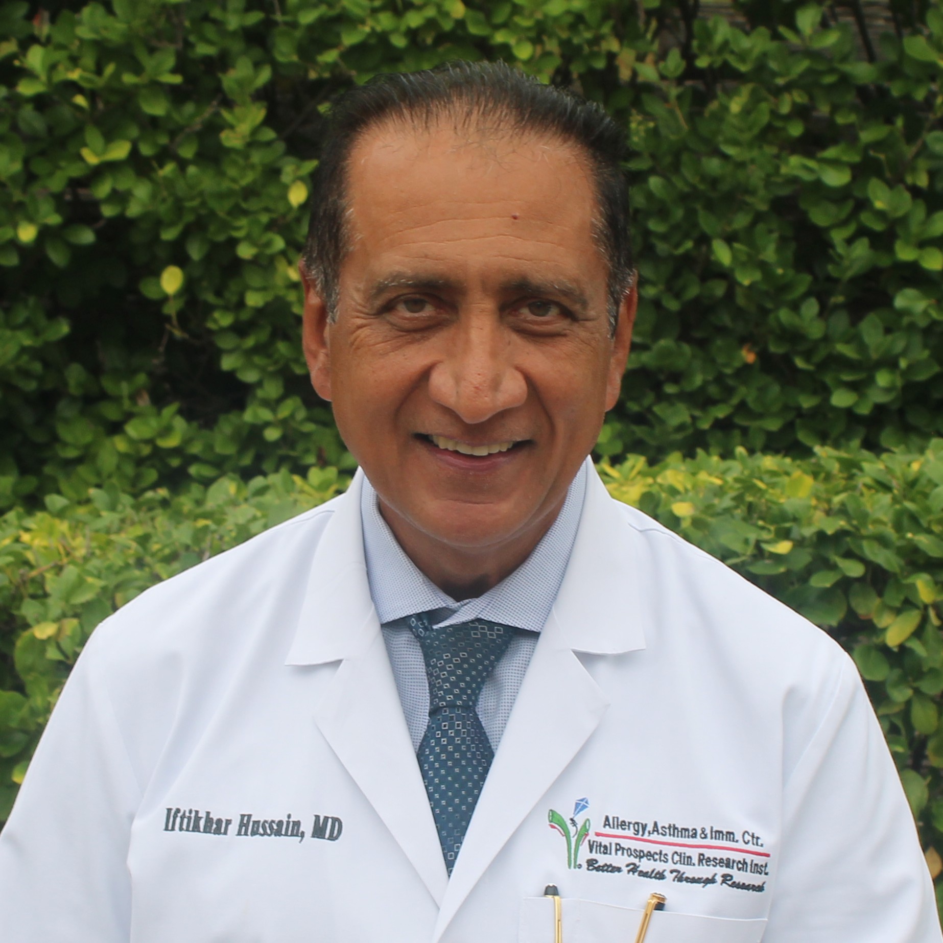 Dr. Iftikhar Hussain, MD, Founder and Owner of Mind Rejuvenation, smiling outdoors in a white medical coat. Featured on the Meet Our Team page to reflect leadership, clinical expertise, and compassionate care in mental wellness.