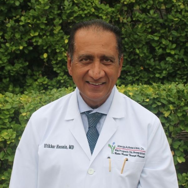 Dr. Iftikhar Hussain, MD, Founder and Owner of Mind Rejuvenation, smiling outdoors in a white medical coat. Featured on the Meet Our Team page to reflect leadership, clinical expertise, and compassionate care in mental wellness.